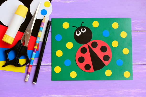 Bright ladybug cardboard card. Green card with ladybug, scissors, glue stick, pencil, marker, cardboard set on a wooden table. Summer homemade card idea to make. Closeup