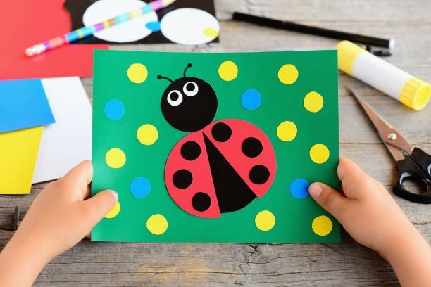 istock Small child holds a ladybug card in his hands. Child created a cardboard ladybug card. Stationery on a desk. Cardboard circle crafts for teaching kids to cut and glue. Developing children motor skills 696877580