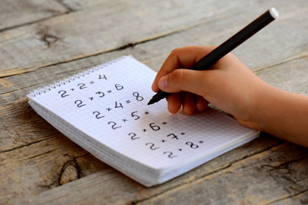 istock Child solves mathematics examples. Child holds a black marker in his hand. Notebook sheet with multiplication table examples. Studying a multiplication table concept 696877582