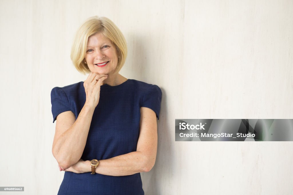 Closeup Portrait of Happy Attractive Senior Woman Closeup portrait of smiling attractive senior business woman looking at camera, touching chin and standing. Isolated front view on light background. Active Seniors Stock Photo