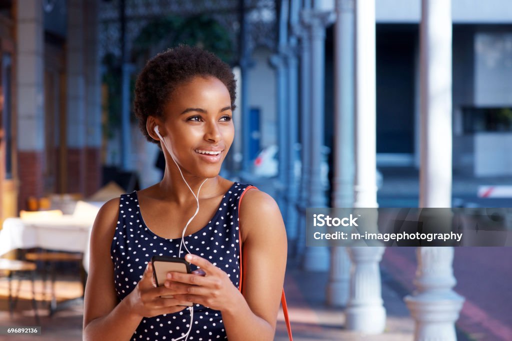 elegant young black woman listening to music with smart phone Portrait of elegant young black woman listening to music with smart phone and earphones 20-29 Years Stock Photo