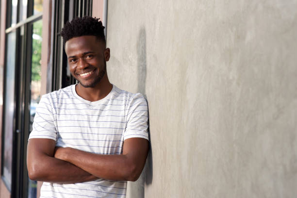 istock attractive young african man leaning on wall with arms crossed 696892216