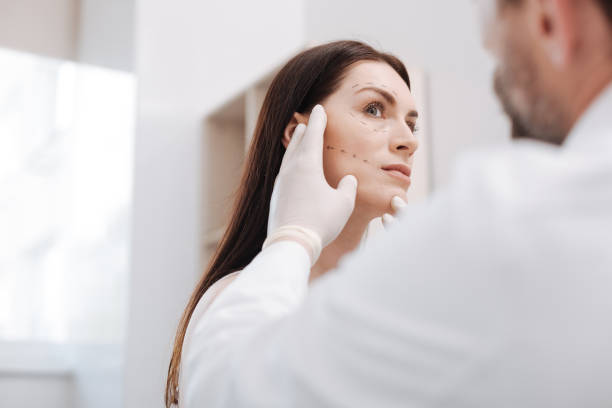 Diligent bright plastic surgeon in the middle of the process Before injections. Neat thorough qualified doctor planning the lifting procedure by drawing the guidelines on patient face he following during the surgery female sharp shooter stock pictures, royalty-free photos & images