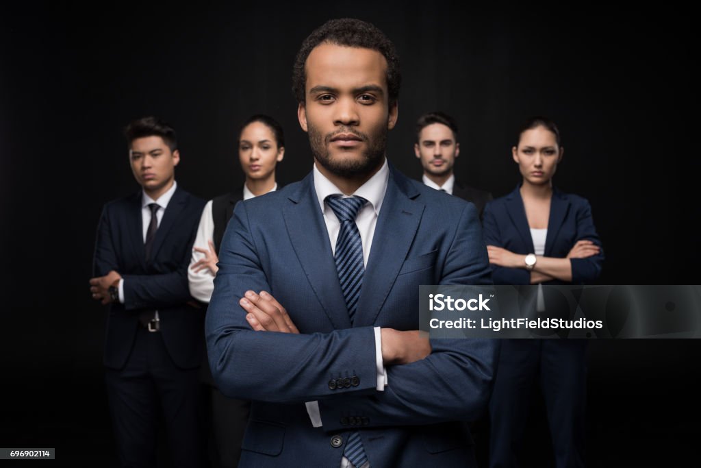 Serious businessman with his business colleagues standing with arms crossed and looking at camera isolated on black Arms Crossed Stock Photo