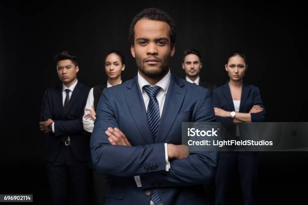 Serious Businessman With His Business Colleagues Standing With Arms Crossed And Looking At Camera Isolated On Black Stock Photo - Download Image Now