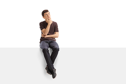 Pensive teenager sitting on a panel isolated on white background