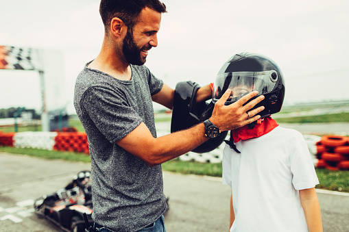 Father and son go-Karts together. Mother putting crash helmet on her head.