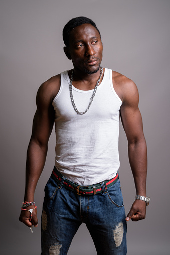 Studio shot of young muscular handsome African man wearing tank top against gray background vertical shot