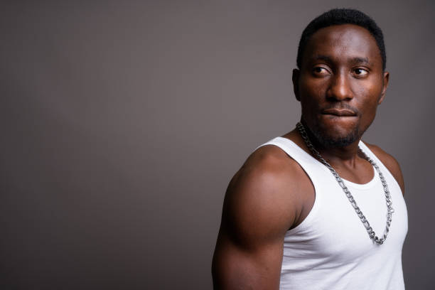 studio shot of young muscular handsome african man wearing tank top against gray background - biting lip imagens e fotografias de stock