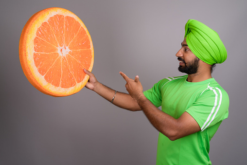 Studio shot of young Indian Sikh man wearing green turban against gray background horizontal shot