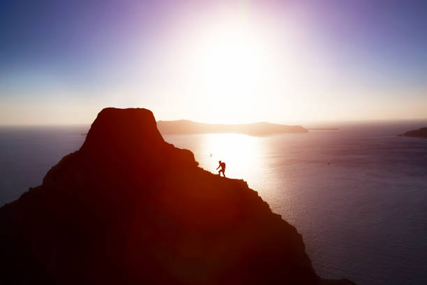 man climbing up hill to reach the peak of the mountain over ocean. - colina acima imagens e fotografias de stock