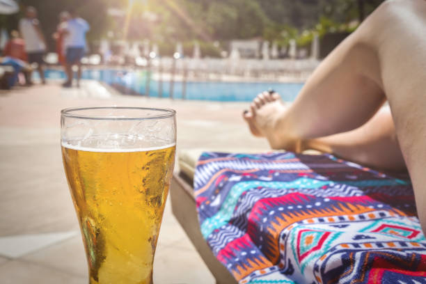 Woman with beer resting on sun bed against swimming pool