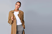 Confident young woman holding brown trench coat