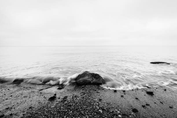Nostalgic sea. Waves hitting in rock in the center. Black and white, far horizon.
