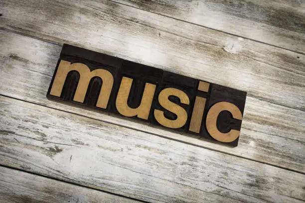 The word "music" written in wooden letterpress type on a white washed old wooden boards background.