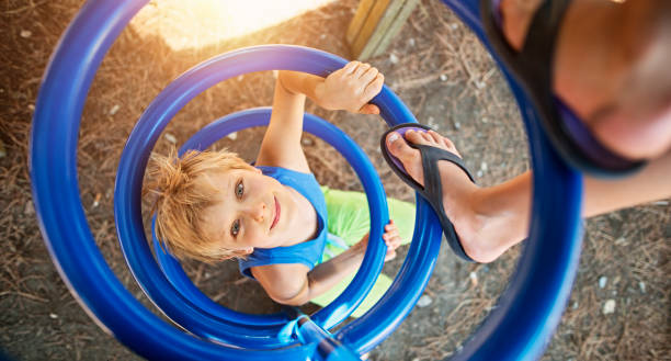 Little boy aged 7 is playing in playground. He is climbing spiral element. Feet of his siter visible.