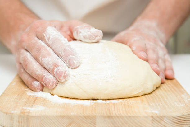 istock Chef's hands kneading the dough on the wooden board. Preparation for baking. 696977260
