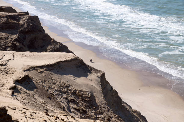 pareja caminando en la playa de rubjerg knude contra las dunas de arena - løkken fotografías e imágenes de stock