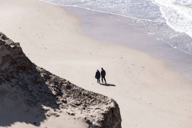 pareja caminando en la playa de rubjerg knude contra las dunas de arena - løkken fotografías e imágenes de stock