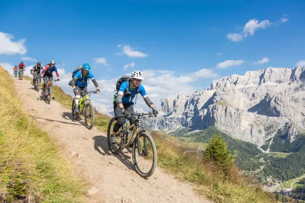 Six fully equipped and experienced mountainbikers are lined up in a row on a scenic downhill in the Dolomites with spactacular scenery. The region is popular for skiing in wintertime and hiking and mountainbiking in summertime. In August 2009, the Dolomites were declared a UNESCO World Heritage Site.
