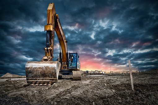 Excavator machinery at construction site, sunset in background.