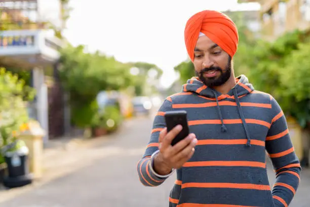 Portrait of young Indian Sikh man wearing hoodie and orange turban in the streets outdoors horizontal shot