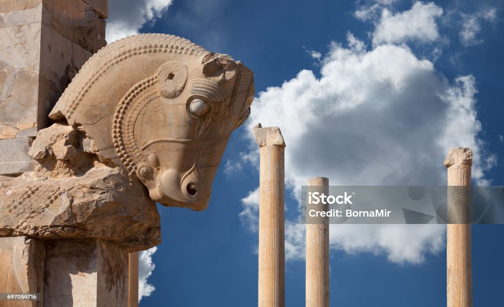 Persian Column with Bull Capital Against Blue Sky with White Fluffy Clouds from Persepolis of Shiraz in Iran Bull figure used as decorative capital statuary of a column in Persepolis of Shiraz against blue sky with white fluffy clouds. Architectural Column Stock Photo