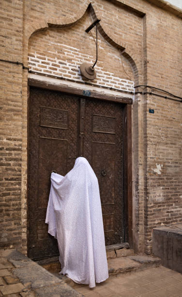 Woman in Veil Knocking on the Old Wooden Door of a Building in Yazd of Iran stock photo