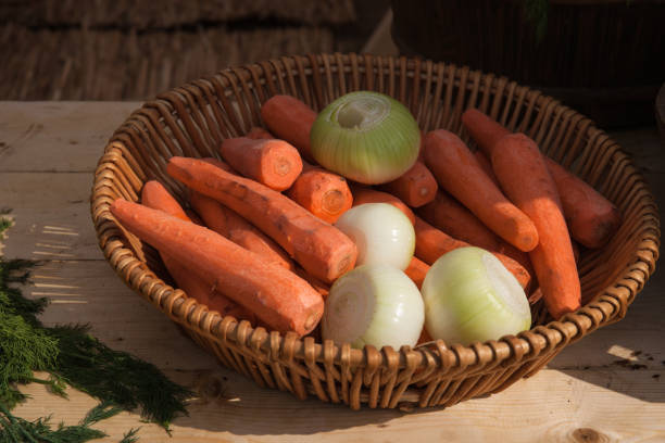 Peeled off carrot and onion vegetables in a wicker bowl, a pile of fennel or dill on a wooden table.