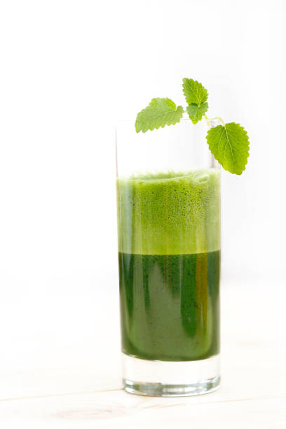 Green vegetable juice in a tall glass with a leaf of kale and mint