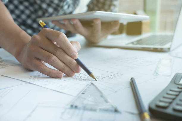 istock Architect working on real estate project at workplace. Male engineer hand working with digital tablet and living house blueprint at office. Business, people, construction and building concept 697122974