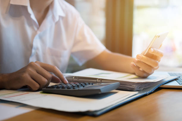 istock Businessman at desk using calculator and financial app on his smart phone working on reports 697127272