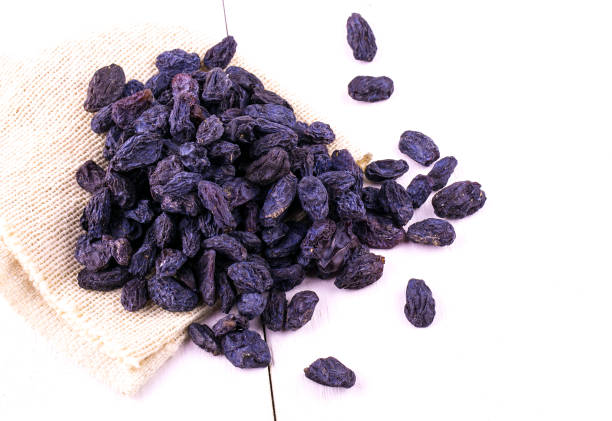 istock Blue raisins scattered on sackcloth on a white wooden table. 697134314