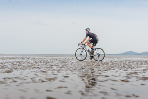 Young asian cyclist man ride  bicycle  the beach at the sunset