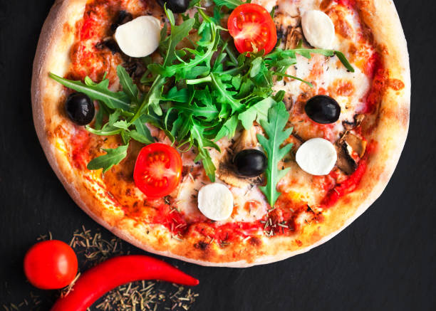istock Rustic pizza with mozzarella, four cheese, olives and arugula  top view with copy space for restaurant menu on black background. 