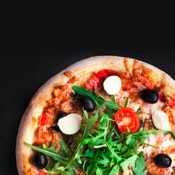 istock Rustic pizza with mozzarella, four cheese, olives and arugula  top view with copy space for restaurant menu on black background. 697173758
