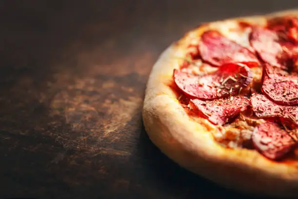 Photo of Pizza with pepperoni and salami on a rustic wooden table.