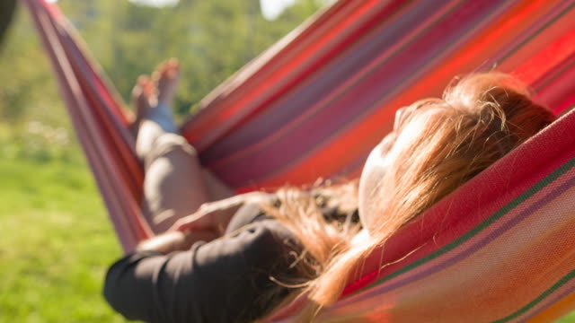 Woman sleeping in a swinging hammock in backyard at sunrise