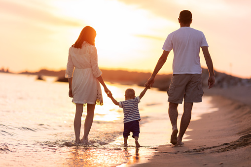 Mother and father walking on beach with their baby boy and enjoying at sunset