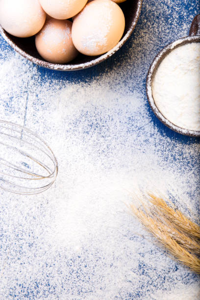 istock Fresh eggs in a bowl, eggbeater, wheat on flour background. Top view. Copy space. 697217848