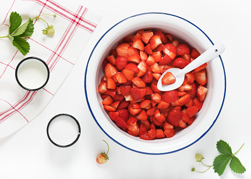 Small pieces of freshly harvested strawberries served in a white enamel plate with milk and sugar. Top view.