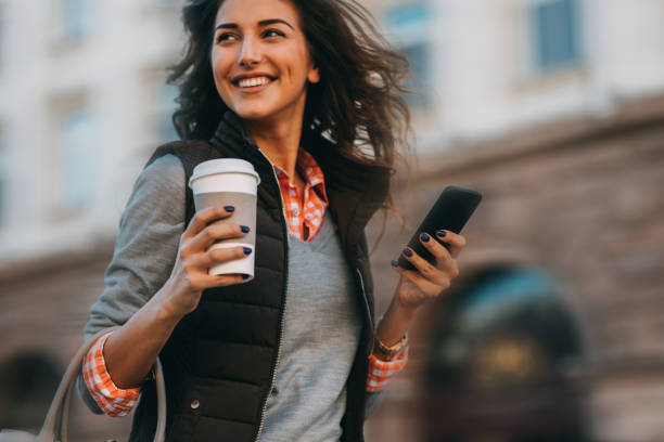Woman texting and drinking coffee outdoors.