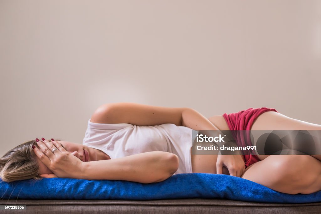 Young beautiful woman with long hair sleeping curl up on the brown bed with stomach Ache because menstrual pain soft focus background Young beautiful woman with long hair sleeping curl up on the brown bed with stomach Ache because menstrual pain soft focus background. Young sick woman with hands holding pressing her crotch lower abdomen. Medical or gynecological problems, healthcare concept Vagina Stock Photo