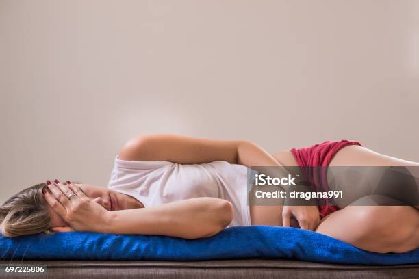 Young Beautiful Woman With Long Hair Sleeping Curl Up On The Brown Bed With Stomach Ache Because Menstrual Pain Soft Focus Background Stock Photo - Download Image Now