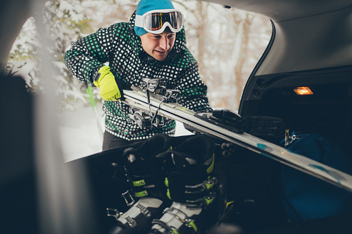 Young man packing his skis in the trunk of the car