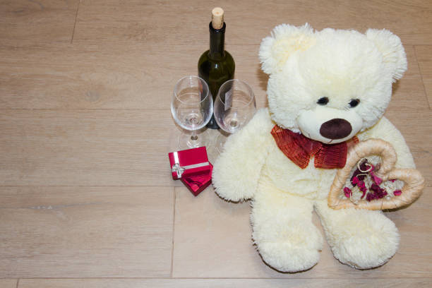 Teddy bear with gifts and love heart, and near glasses and a bottle of wine.