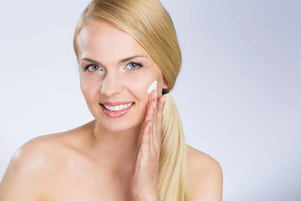 istock Happy woman applying cream on face 697236012