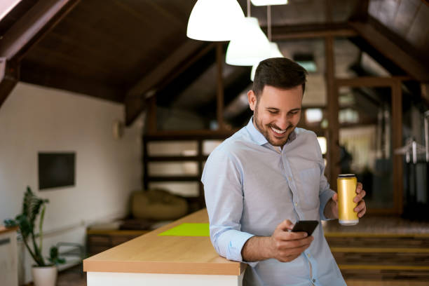 istock Happy man with smartphone drinking beer and reading message at home. 697236474