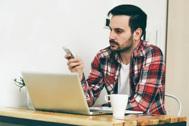 istock Young businessman using smartphone while sitting in home office, in front laptop. 697248440