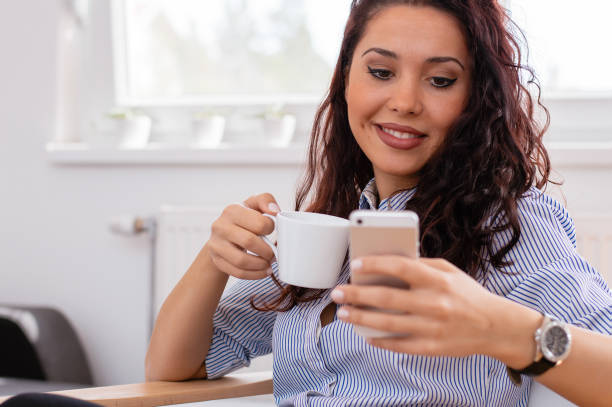 istock Young woman at home drinking coffee and using mobile phone 697248592